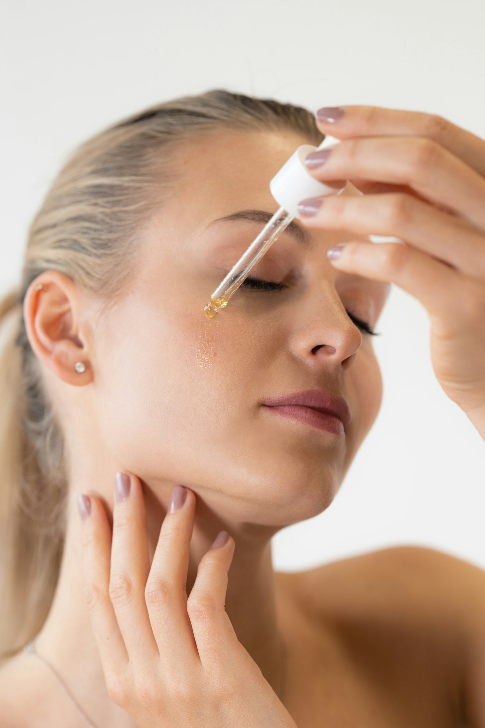 Frau trägt PDRN Serum mit einer Pipette auf die Gesichtshaut auf